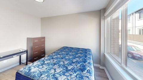 A bedroom with a blue bedspread and a window overlooking a parking lot.